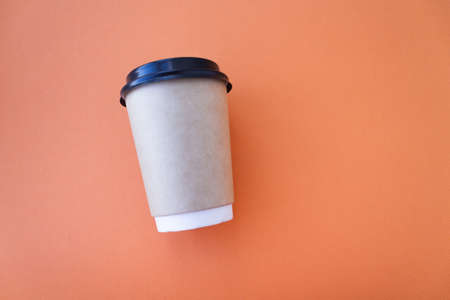 Coffee to go concept. Disposable craft cup with black plastic cover on a trendy orange background. Place for text. Flat lay style. Top viewの写真素材