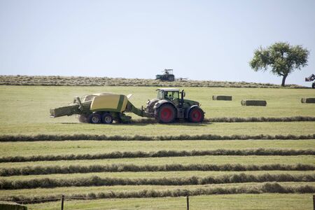 Tractor at work on field making haystacksの写真素材