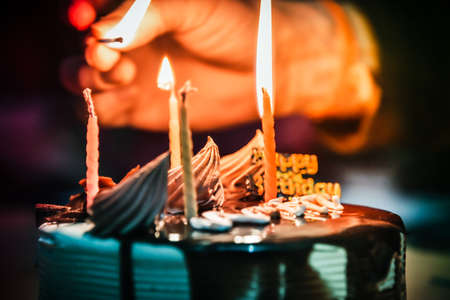 Close view of lighting candles with matchstick on a chocolate cake.の写真素材