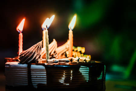 Close view of burning candles on a cake with dark background.の写真素材