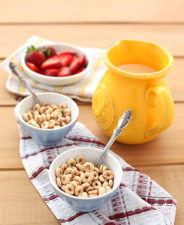 Close-up of a two bowls of cereal with a pitcher of fresh milk and strawberries.  Served on a wooden table, with a metal spoon on a napkin.の写真素材