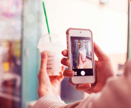 Closeup taking a picture of a cup of frappuccino with cell phone  Toned imageの写真素材