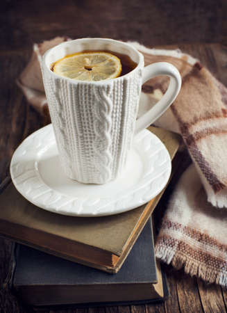 Cup of hot tea with lemon, books and scarf on wooden tableの写真素材