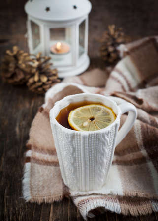 Cup of hot tea with lemon and scarf on wooden tableの写真素材