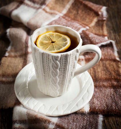 Cup of hot tea with lemon and scarf on wooden tableの写真素材