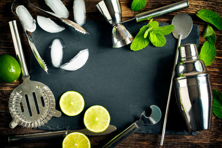 Set of bar accessories and ingredients for making a cocktails arranged on a wooden background with black board for copy spaceの写真素材