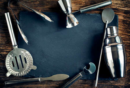 Set of bar accessories and ingredients for making a cocktails arranged on a wooden background with black board for copy spaceの写真素材
