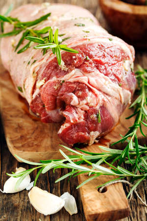 Raw boneless lamb leg with garlic and rosemary on wooden background.の写真素材