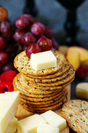 Cheddar cheese, creckers and fruits on wooden boardの写真素材