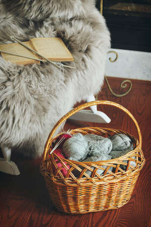 Basket with balls of yarn near chair. Selective focus on knitting needles