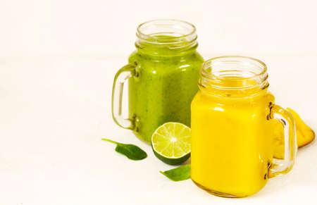 Green Spinach Avocado Smoothie and Banana Mango Smoothie in mason jars. Healthy vegan eating.の写真素材