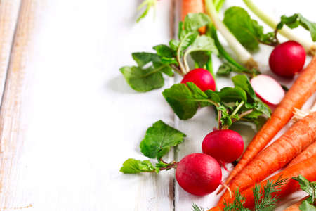 Spring vegetables on white wooden background with copy space. Carrots, radish and green onion - fresh harvest from the garden.の写真素材