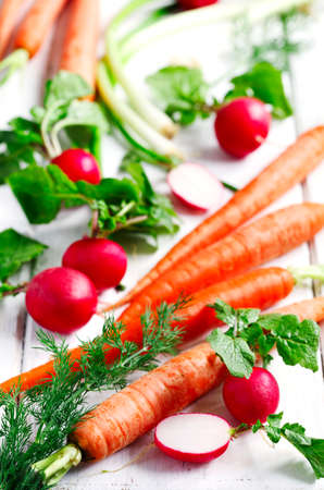 Spring vegetables on white wooden background. Carrots, radish, green onion and dill - fresh harvest from the garden.の写真素材