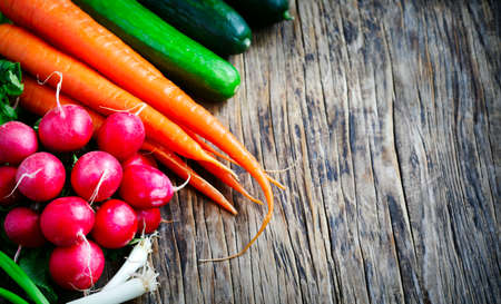 Spring vegetables on wooden background with copy space. Carrots, radish, cucumber and green onion - fresh harvest from the garden.の写真素材