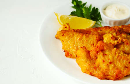 Golden batter deep fried fish fillets, served on white plate with sauce and lemonの写真素材