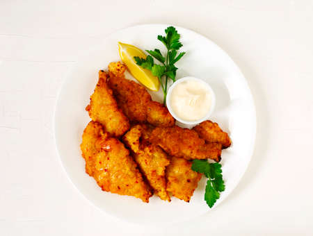 Golden batter deep fried fish fillets, served on white plate with sauce and lemon, top viewの写真素材