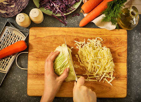 Coleslow salad preparation. Women's hands cut vegetables for salad. Fresh vegetables on kitchen table, top view. の写真素材