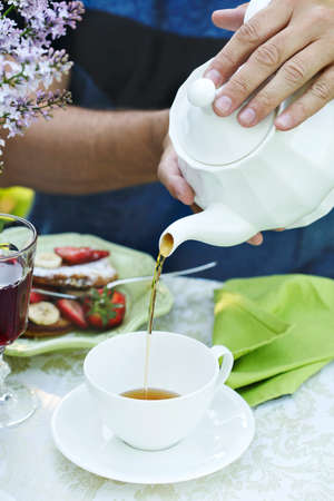 A man pours tea into a cup. Summer breakfast in the gardenの写真素材