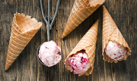 Raspberry vanilla ice cream scoop in a spoon with waffles cones on wooden background, top viewの写真素材