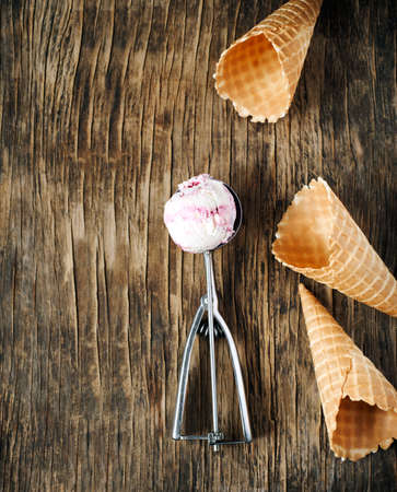 Raspberry vanilla ice cream scoop in a spoon with waffles cones on wooden background with copy spaceの写真素材