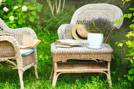 Wicker table, chairs and books in the garden at summer timeの写真素材