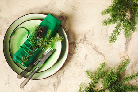 Two green empty round plates with napkin, fork and knife and Christmas decoration - fir tree brunch and cones, top view.の写真素材