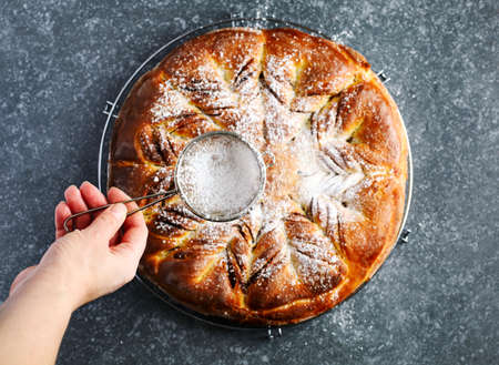 Freshly baked Cinnamon Sweet Brioche. Woman's hand sprinkling powdered sugar freshly baked Sweet Brioche,  top viewの写真素材