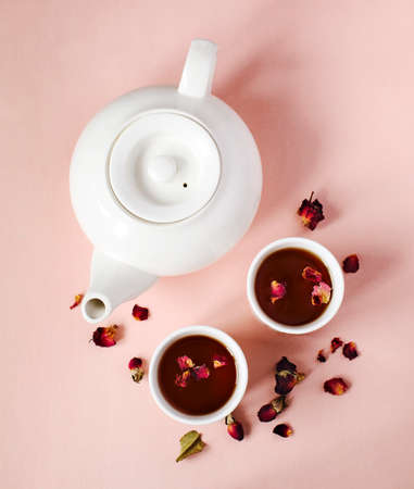 Black tea with rose petals on pink background, top viewの写真素材