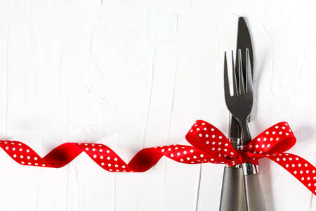 Fork and knife tied with a red ribbon on white background with copy space. Food, restaurant and table setting theme, copy spaceの写真素材