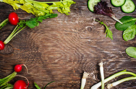 Spring vegetables on wooden background with copy space. Radish, cucumber, green salad, celery and green onion - fresh harvest from the garden.の写真素材