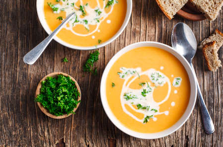 Pumpkin and carrot soup with cream and parsley on wooden background. Top view.の写真素材