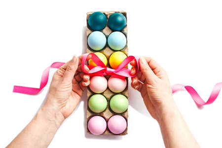 Easter eggs decoration on white background.  Woman's hands decorating with ribbon a box of colorful...