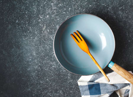 Empty cooking pan and wooden fork on grey stone background, top view, copy spaceの写真素材