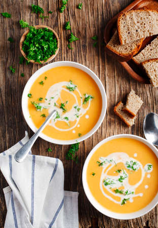 Pumpkin and carrot soup with cream and parsley on wooden background. Top view.の写真素材