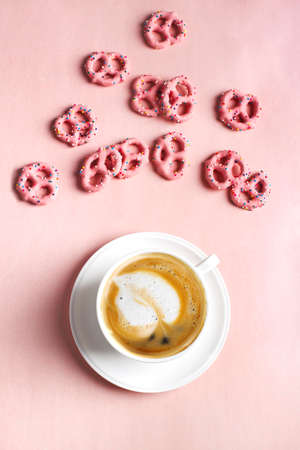 Cup of coffee with art leaf shape and Strawberry flavoured yogurt covered pretzels on pink background. Love concept. Flat lay, top viewの写真素材