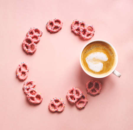 Cup of coffee with art heart shape and Strawberry flavoured yogurt covered pretzels on pink background. Love concept. Flat lay, top viewの写真素材