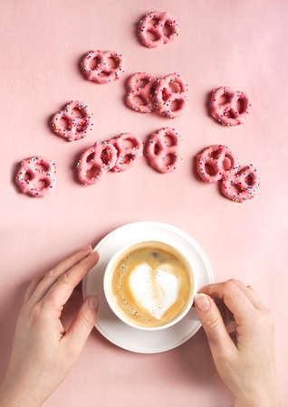 Female hands hold cup of coffee with art heart shape on pink background. Love concept. Flat lay, top viewの写真素材