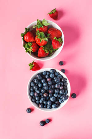 Strawberries and blueberries in bowls on pink background, top view.の写真素材