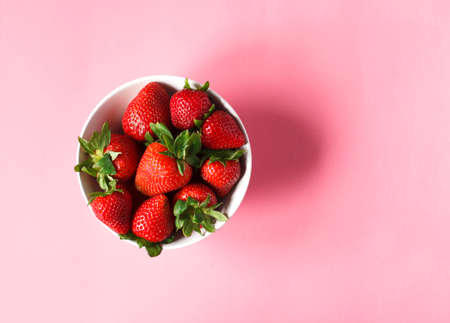 Strawberries in bowls on pink background, top view, copy space