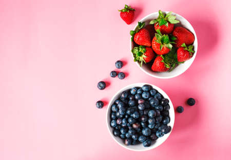 Strawberries and blueberries in bowls on pink background, top view, copy spaceの写真素材