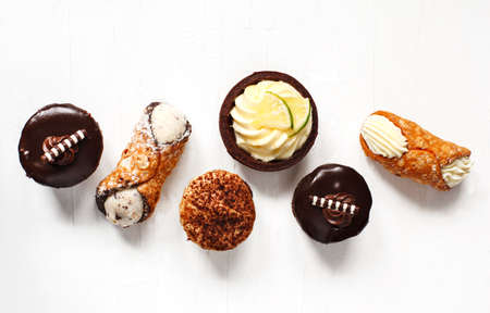 Different pastries on white background: cannoli with ricotta, tartlets filled with citrus cream, fudge cake, tiramisu cake. Top viewの写真素材