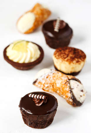 Different pastries on blue background: cannoli with ricotta, tartlets filled with citrus cream, fudge cake, tiramisu cake.の写真素材