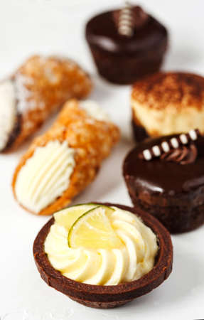Different pastries on blue background: tartlets filled with citrus cream, cannoli with ricotta, fudge cake, tiramisu cake.の写真素材