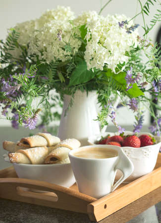 Coffee, rugelach with chocolate filling, strawberries and flowers on wooden tray.の写真素材