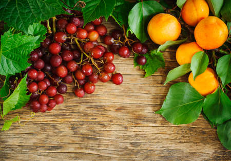 Fresh ripe red grapes and apricots on a wooden background, copy space