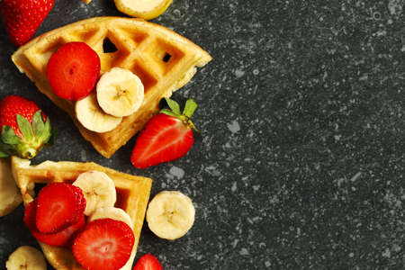 Belgian waffles with strawberries, banana and maple syrup on stone background with copy spaceの写真素材