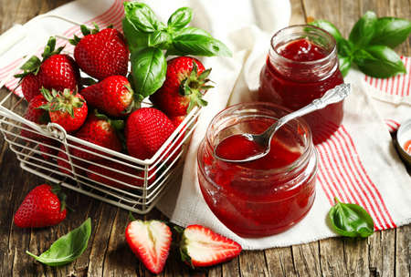 Homemade delicious strawberry jam with basil in a glass jar and fresh strawberries on wooden tableの写真素材