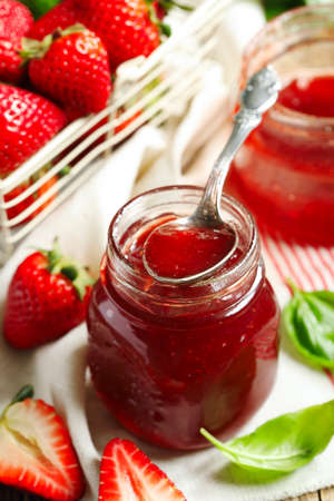 Homemade delicious strawberry jam with basil in a glass jar and fresh strawberries on wooden tableの写真素材