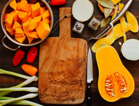 Preparing pumpkin, onions and sweet peppers for cooking around wooden cutting boardの写真素材