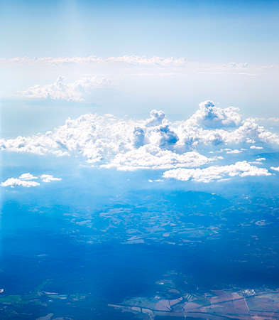 Airplane window view of land and blue sky with white cloudsの写真素材